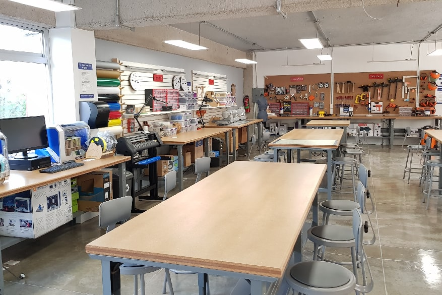 A classroom with pegboards with tools on them, workbenches, and other tools scattered about
